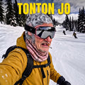Skieur portant le masque de ski rigolo Tonton Jo Yano Mask, cagoule imprimée vieux monsieur aux cheveux gris bouclés avec cigarette, lunettes de ski sur une piste enneigée